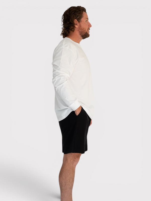 Man wearing a white long-sleeve shirt and black shorts on a plain background