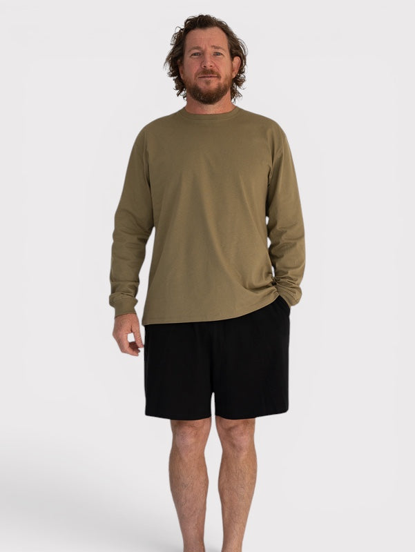 Man wearing a khaki long-sleeve shirt and black shorts on a white background