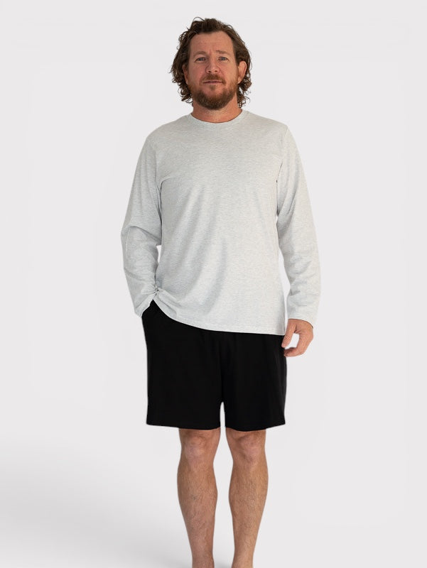 Man wearing a light grey long-sleeve shirt and black shorts on a white background