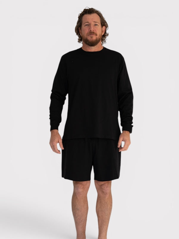 Man wearing a black long-sleeve shirt and black shorts on a white background