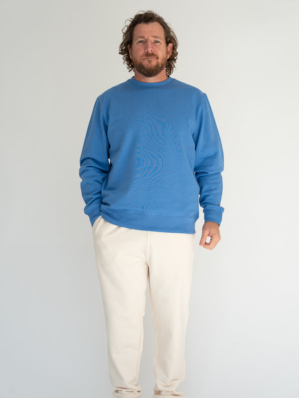 Man wearing a blue sweater and white pants against a plain background