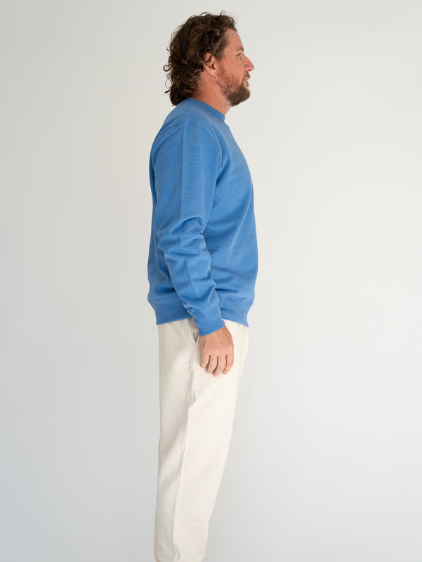 Man wearing a blue sweater and white pants against a plain background
