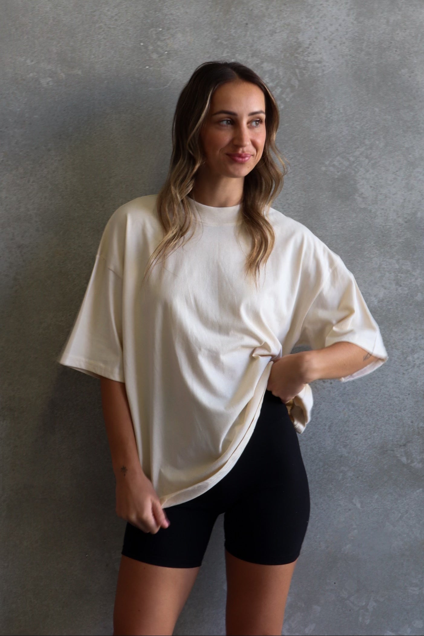 Woman wearing a white oversized t-shirt and black shorts against a gray wall