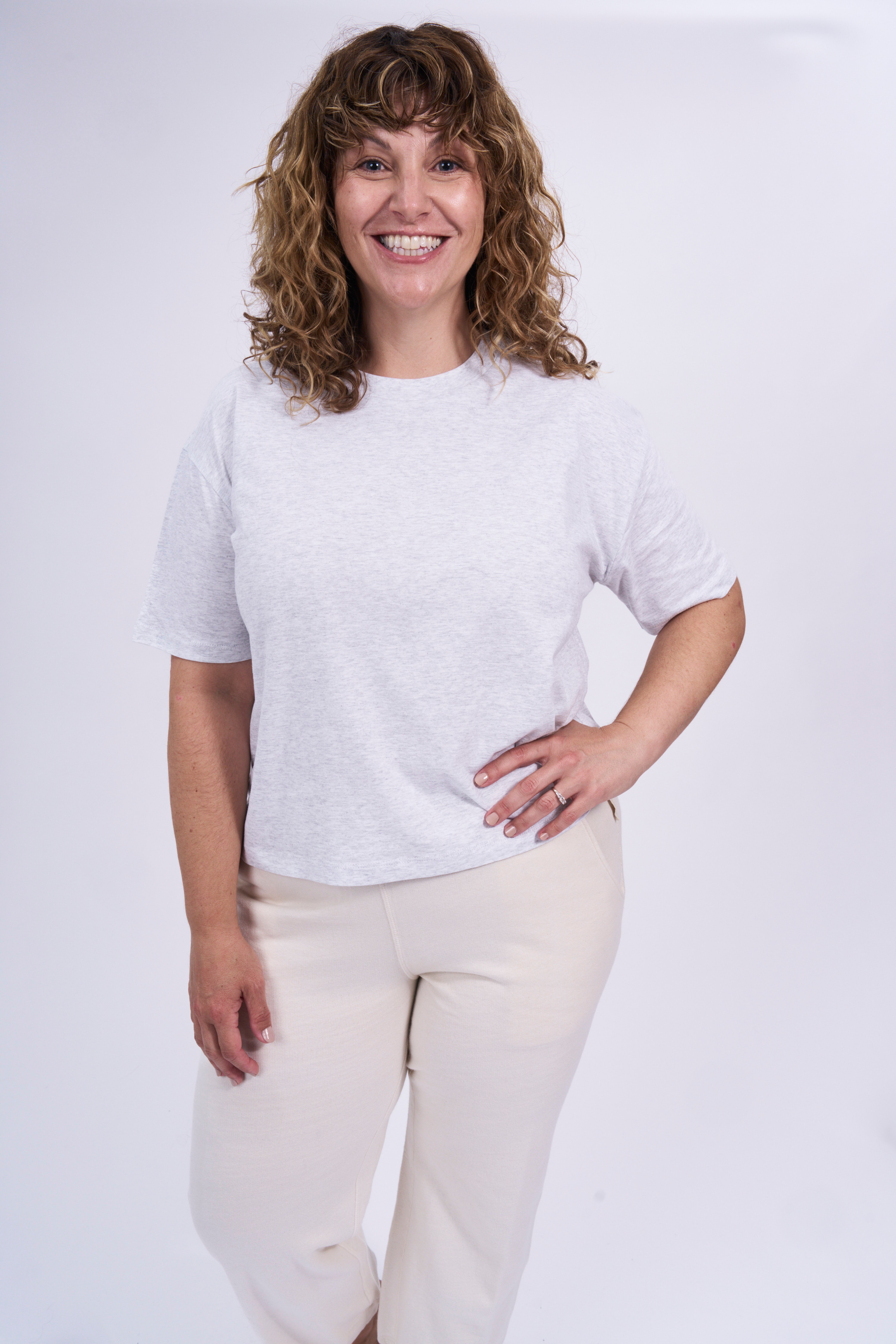Woman wearing a grey organic cotton t-shirt and natural raw pants against a plain background