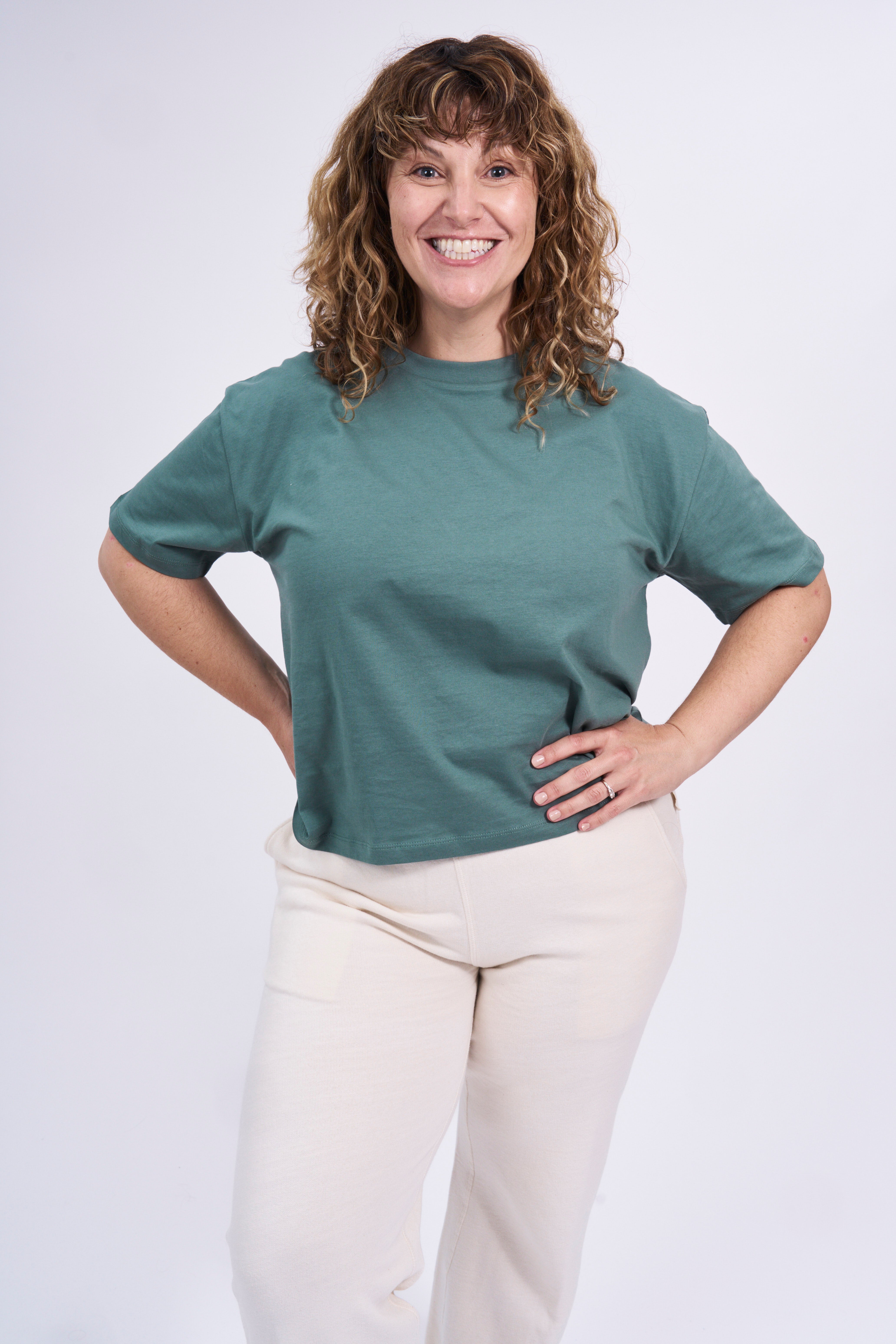 Woman wearing a teal boxy t-shirt and natural raw pants on a white background