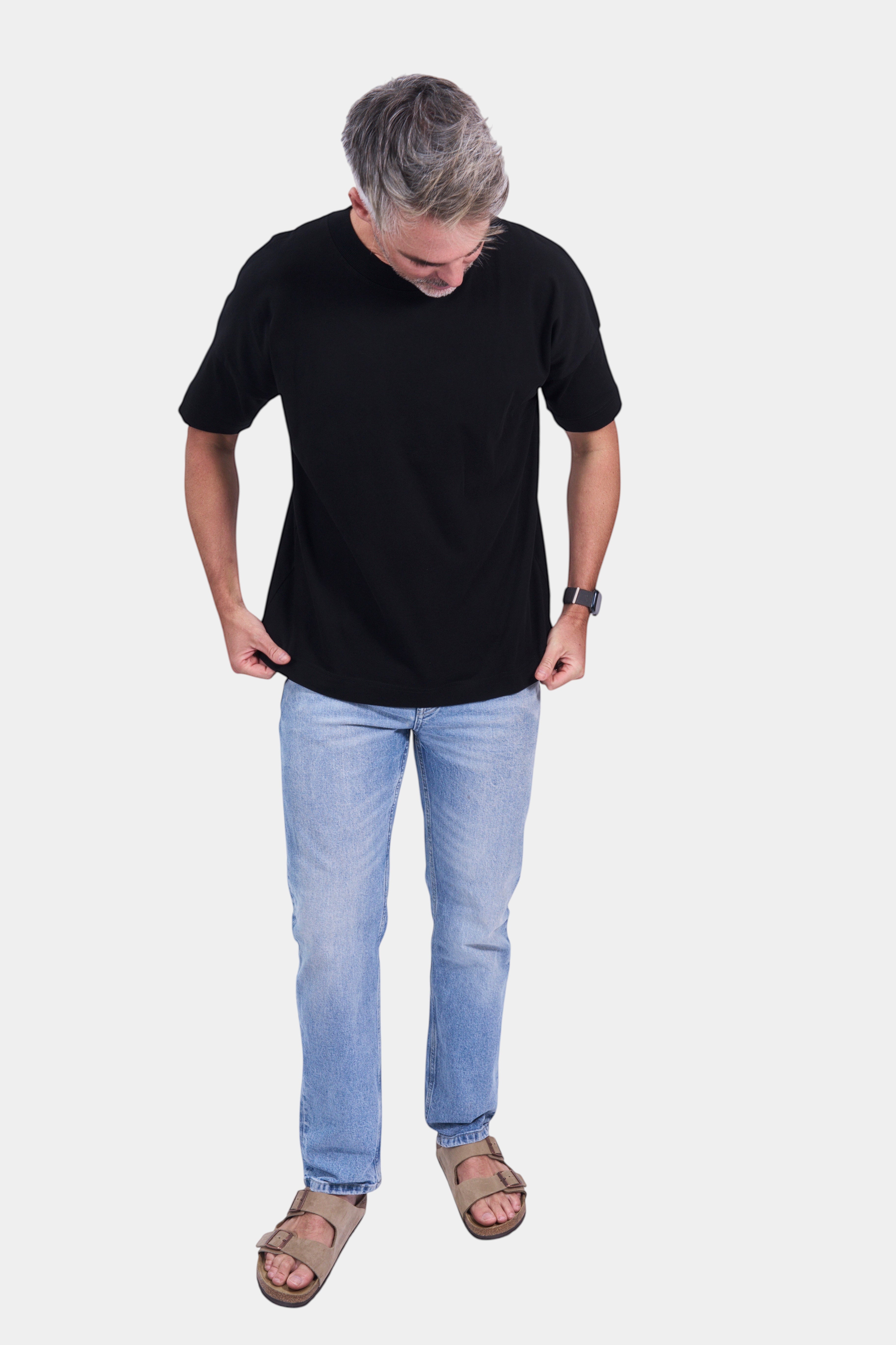 STAPLE Co black organic cotton high neck oversized t-shirt on a man with light wash jeans and sandals.