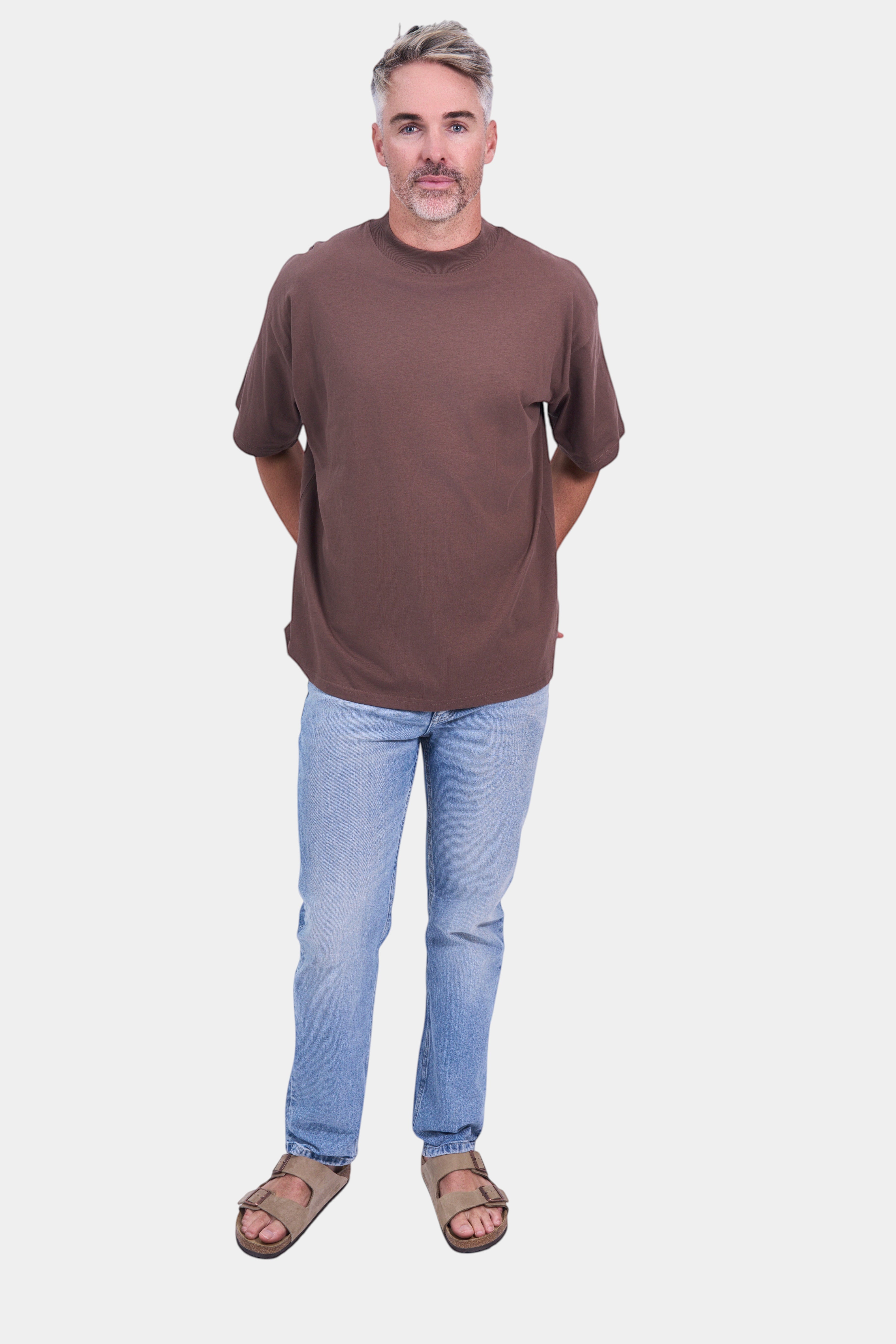 STAPLE Co brown organic cotton high neck oversized t-shirt on a man wearing light wash jeans and sandals.