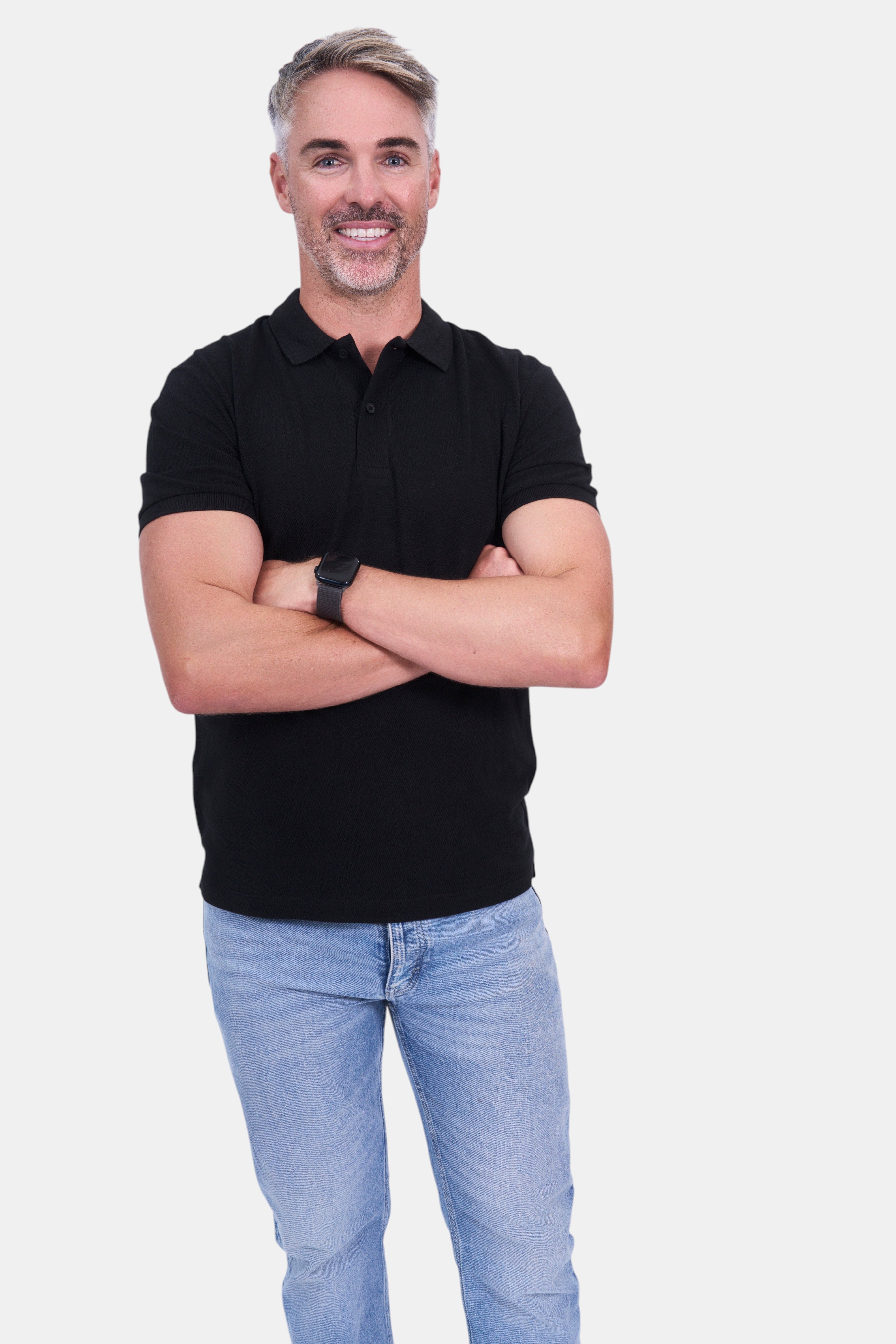 STAPLE Co. black organic cotton polo shirt on a man with arms crossed, wearing light wash jeans.