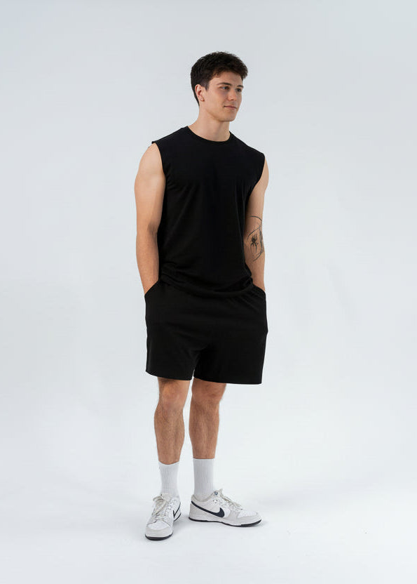 Person wearing a black sleeveless shirt and shorts with white sneakers on a white background
