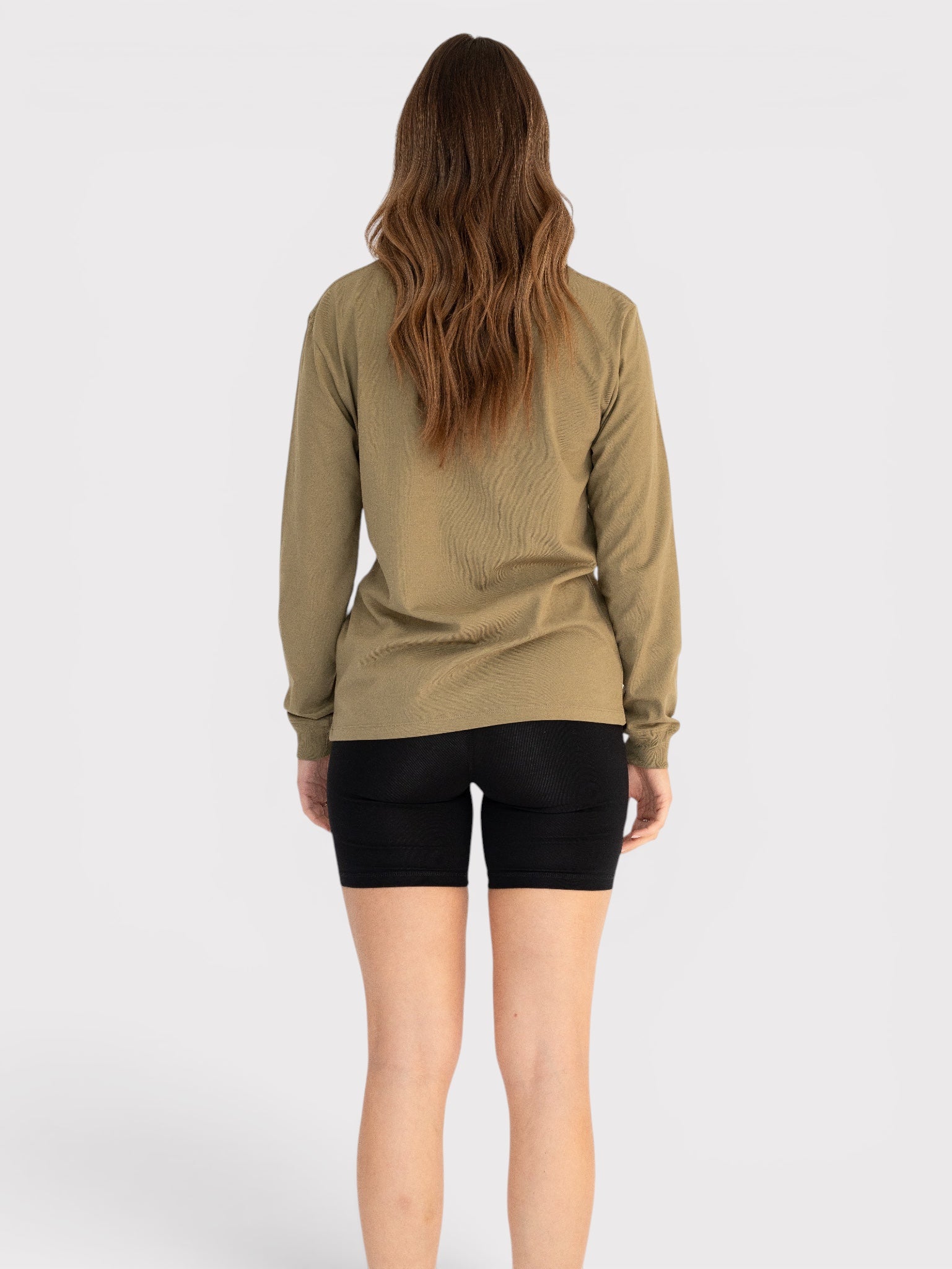 Person wearing a long-sleeve olive green top and black shorts on a white background
