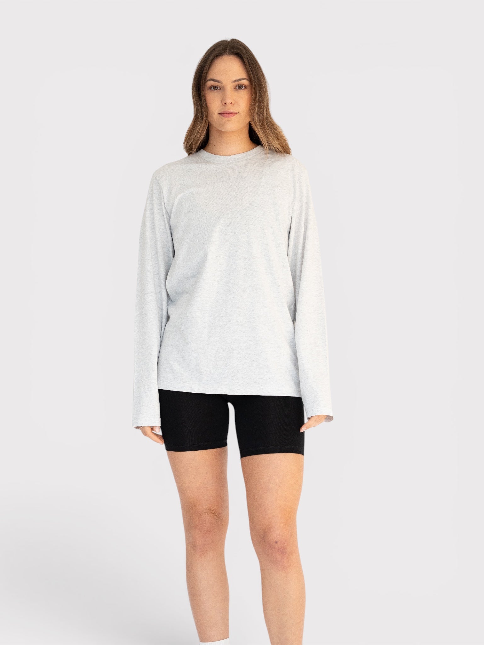 Woman wearing a light grey long-sleeve shirt and black shorts on a white background