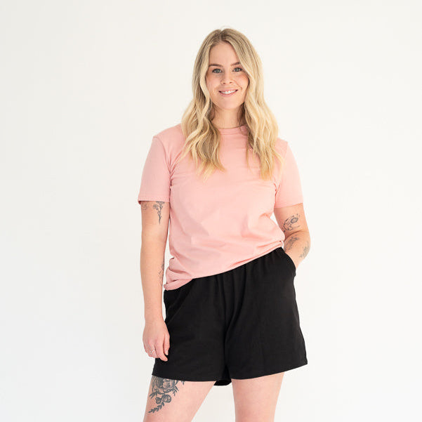 Woman wearing a pink t-shirt and black shorts on a white background