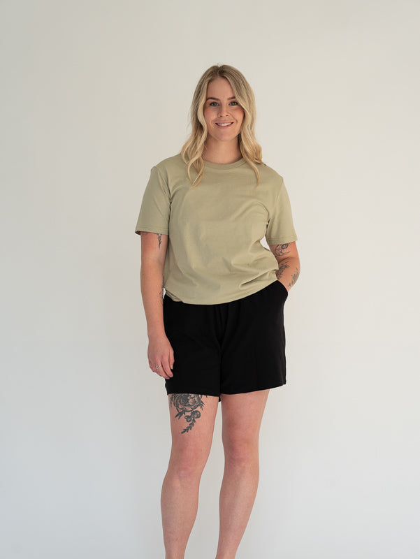 Person wearing a beige t-shirt and black shorts on a white background