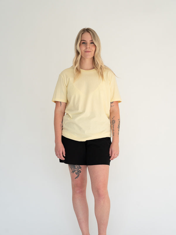 Person wearing a light yellow t-shirt and black shorts on a white background