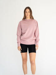 Person wearing a pink sweatshirt and black shorts on a white background