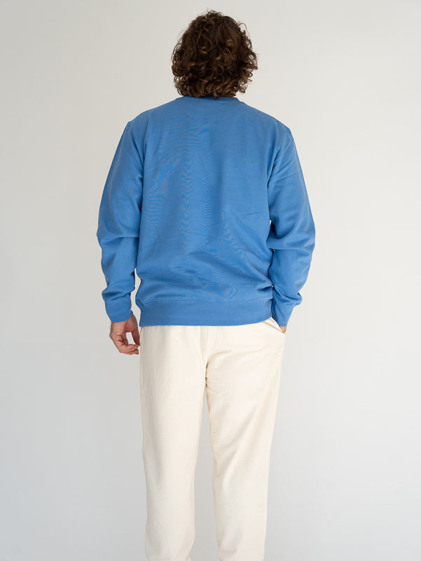 Person wearing a blue sweater and white pants against a plain background
