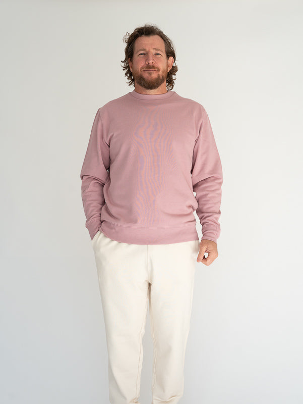 Man wearing a pink sweater and white pants against a plain background