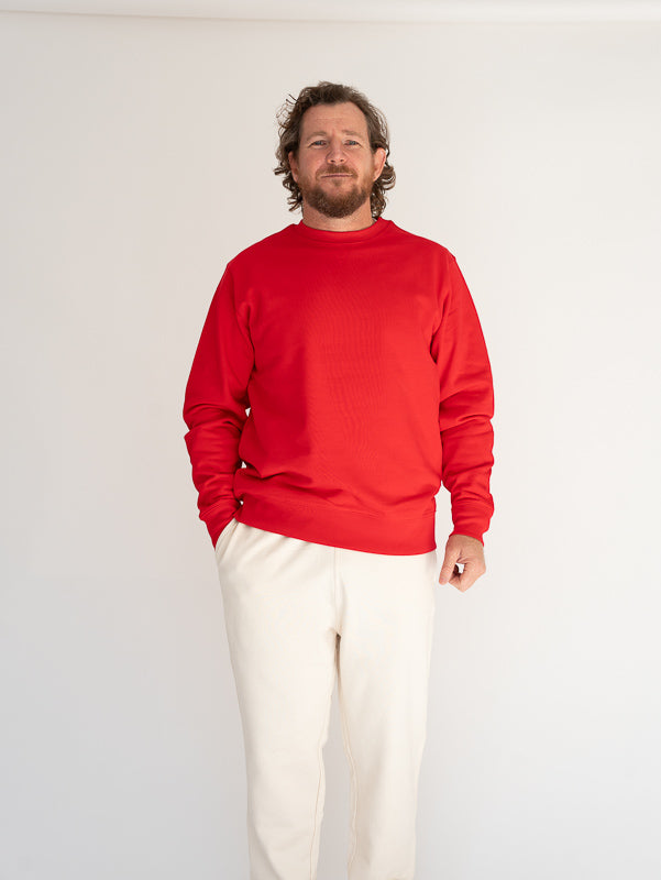 Man wearing a red sweater and white pants against a plain background