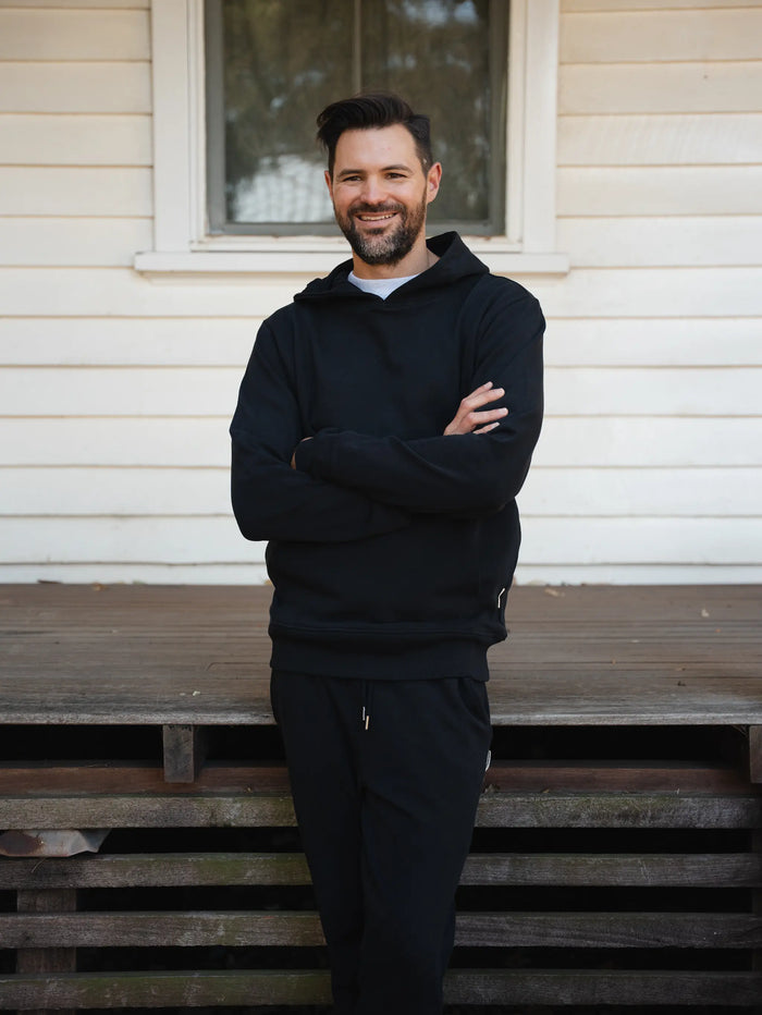 Man wearing a black hoodie and pants standing on wooden steps in front of a house.