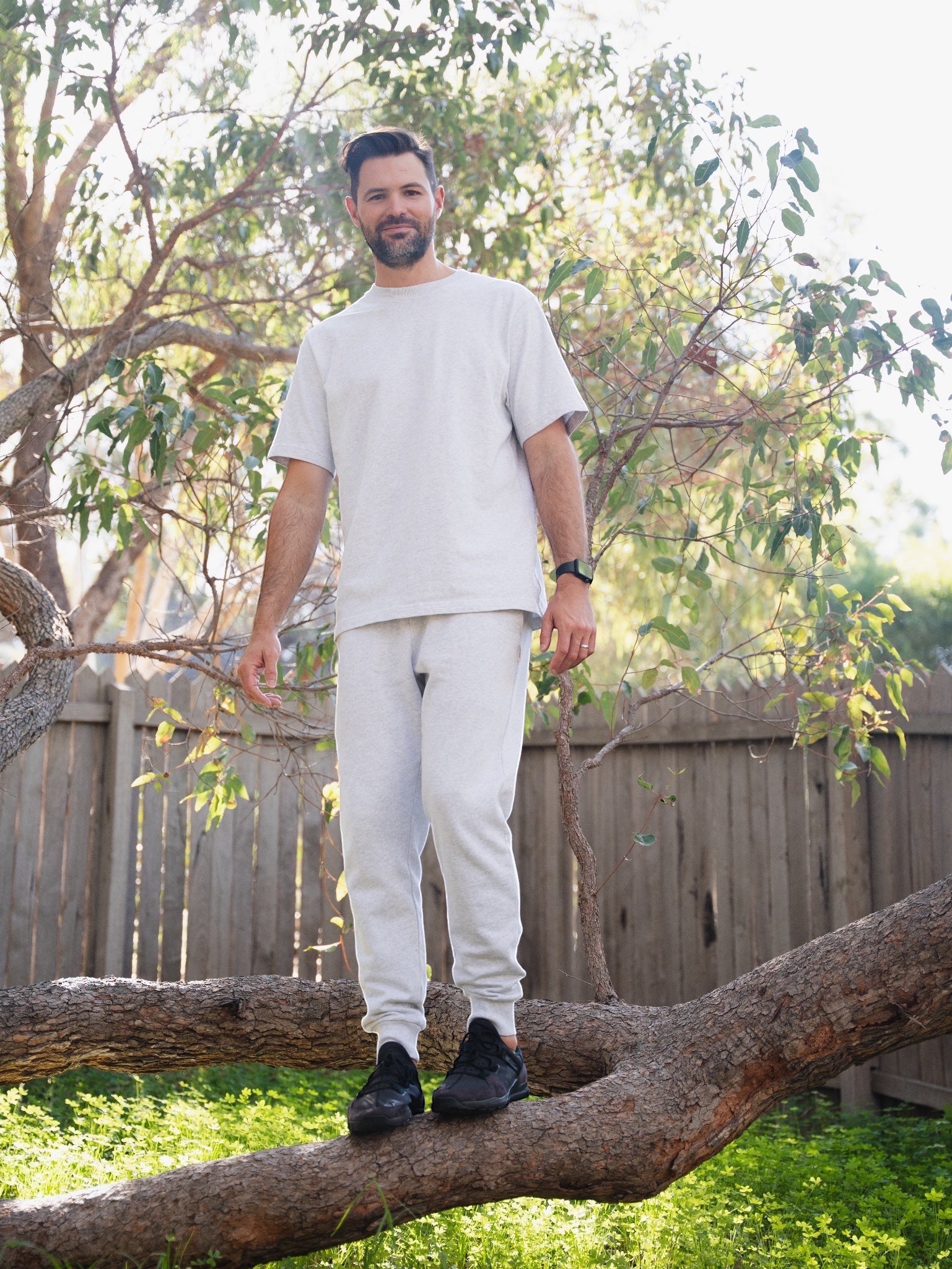 Man standing on a tree branch in a backyard setting