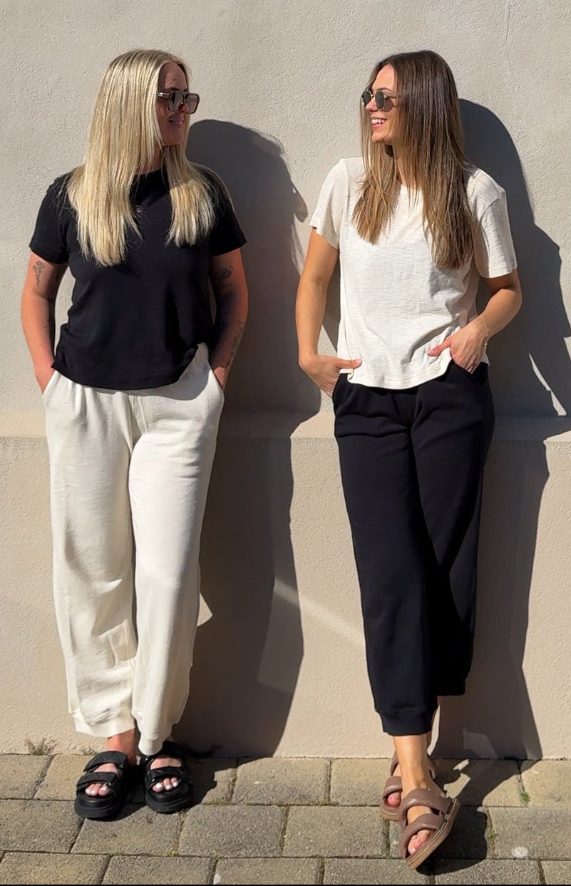 Two women standing against a plain wall, wearing black and white outfits.