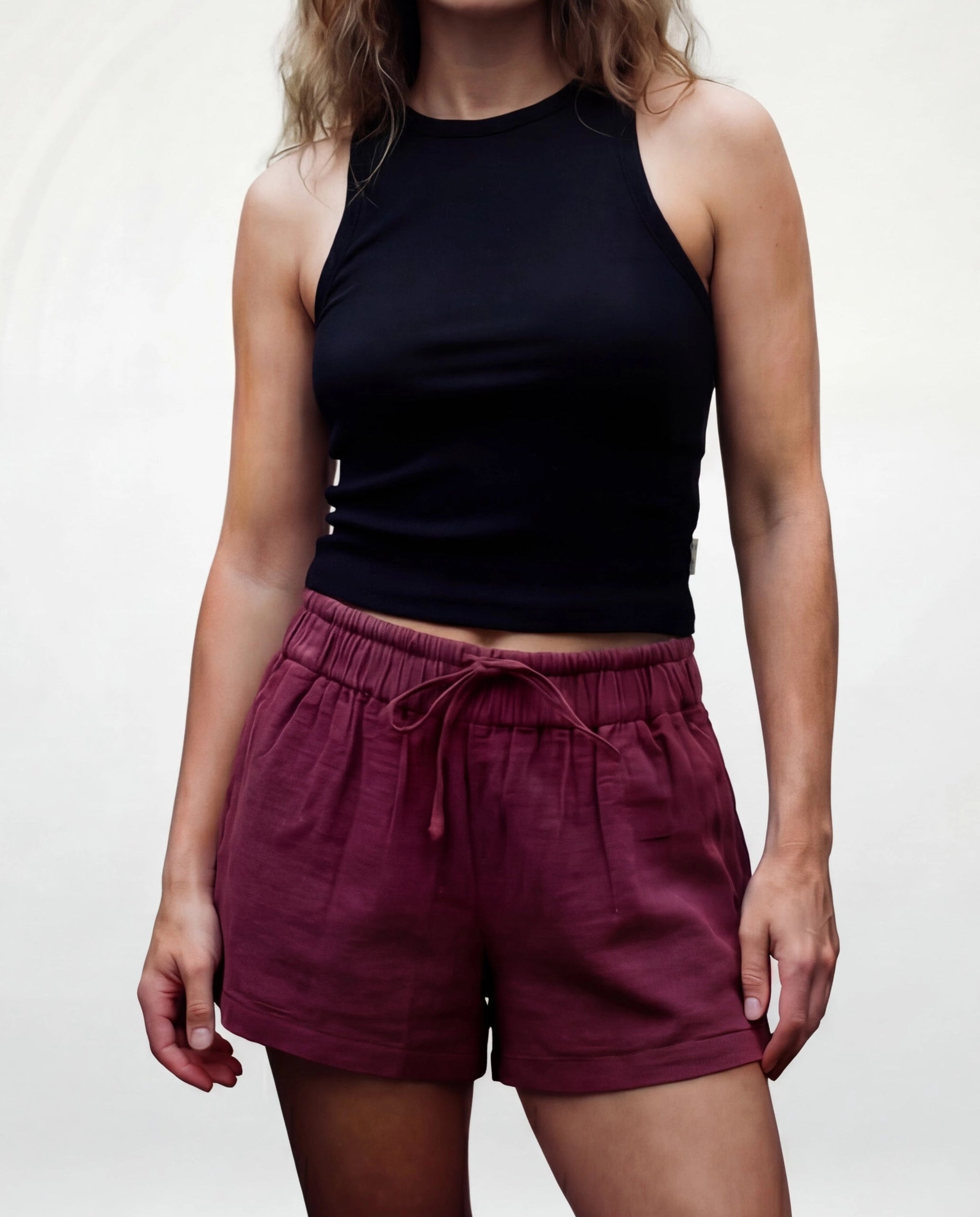 Woman wearing a black sleeveless top and maroon shorts against a plain background