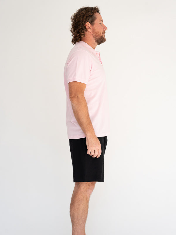 Man wearing a light pink organic cotton polo shirt and black shorts on a white background