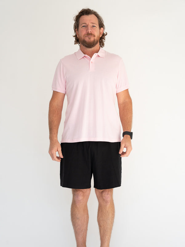 Man wearing a light pink organic cotton polo shirt and black shorts on a white background
