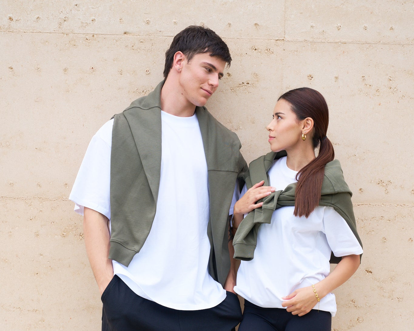 Two people wearing matching outfits with green vests against a beige wall.