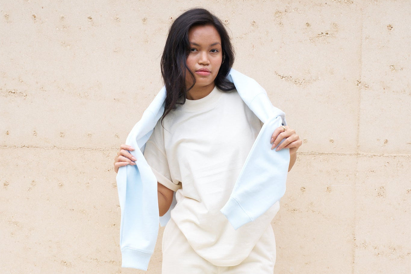 Woman holding a light blue scarf against a beige wall