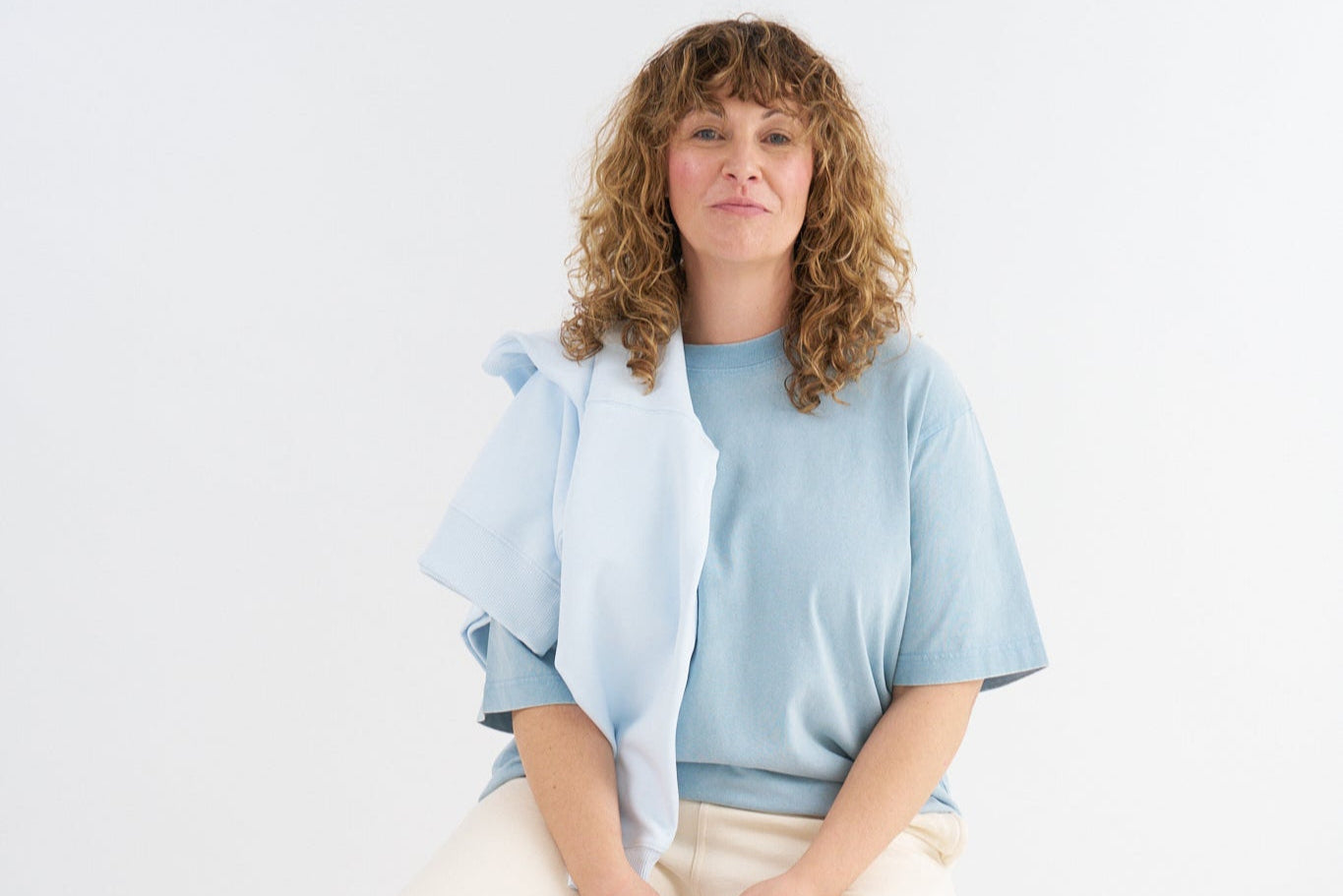 Woman wearing a light blue top and beige pants against a white background
