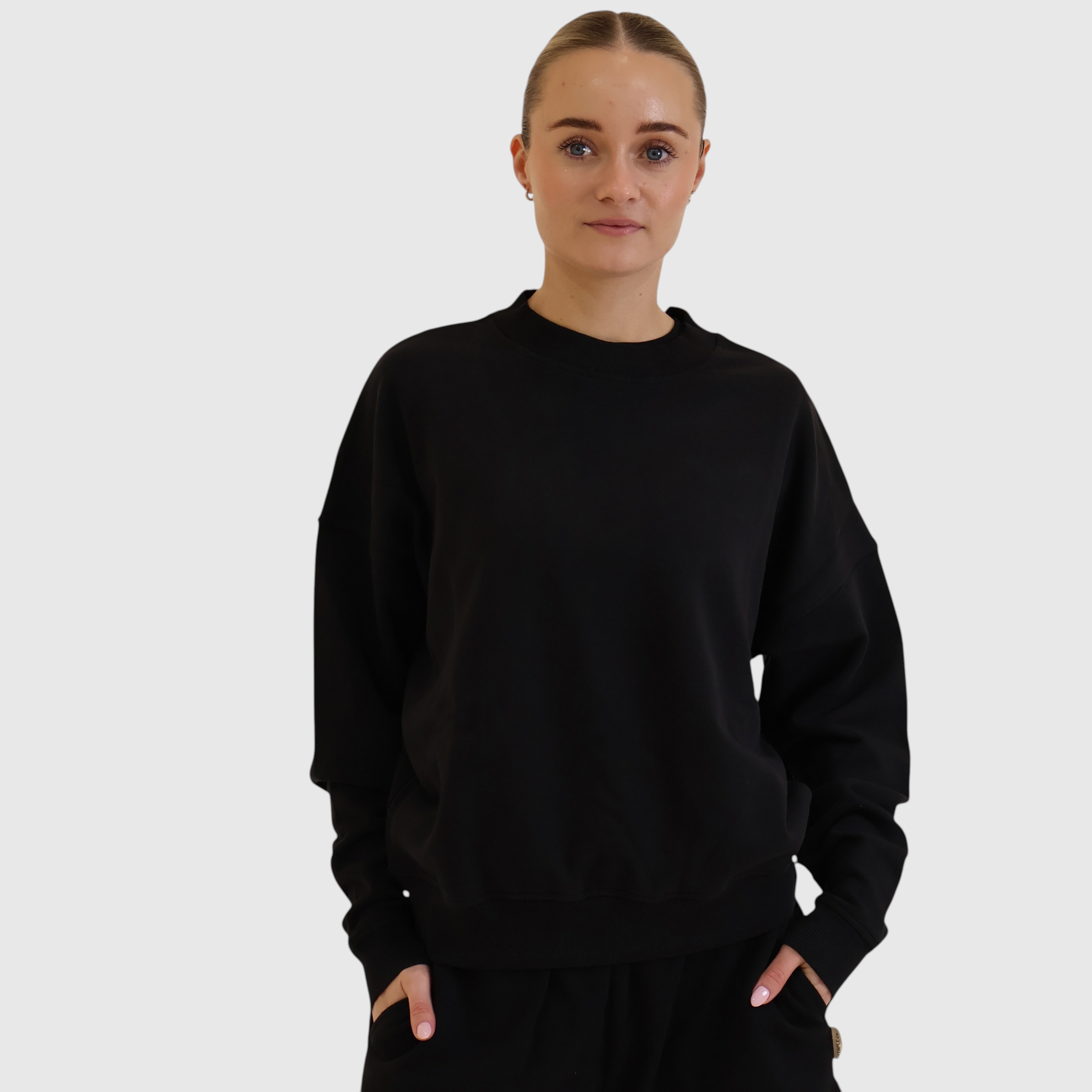 A model wearing a black STAPLE Co crewneck pullover made from soft Regenerative Organic Certified cotton fleece.