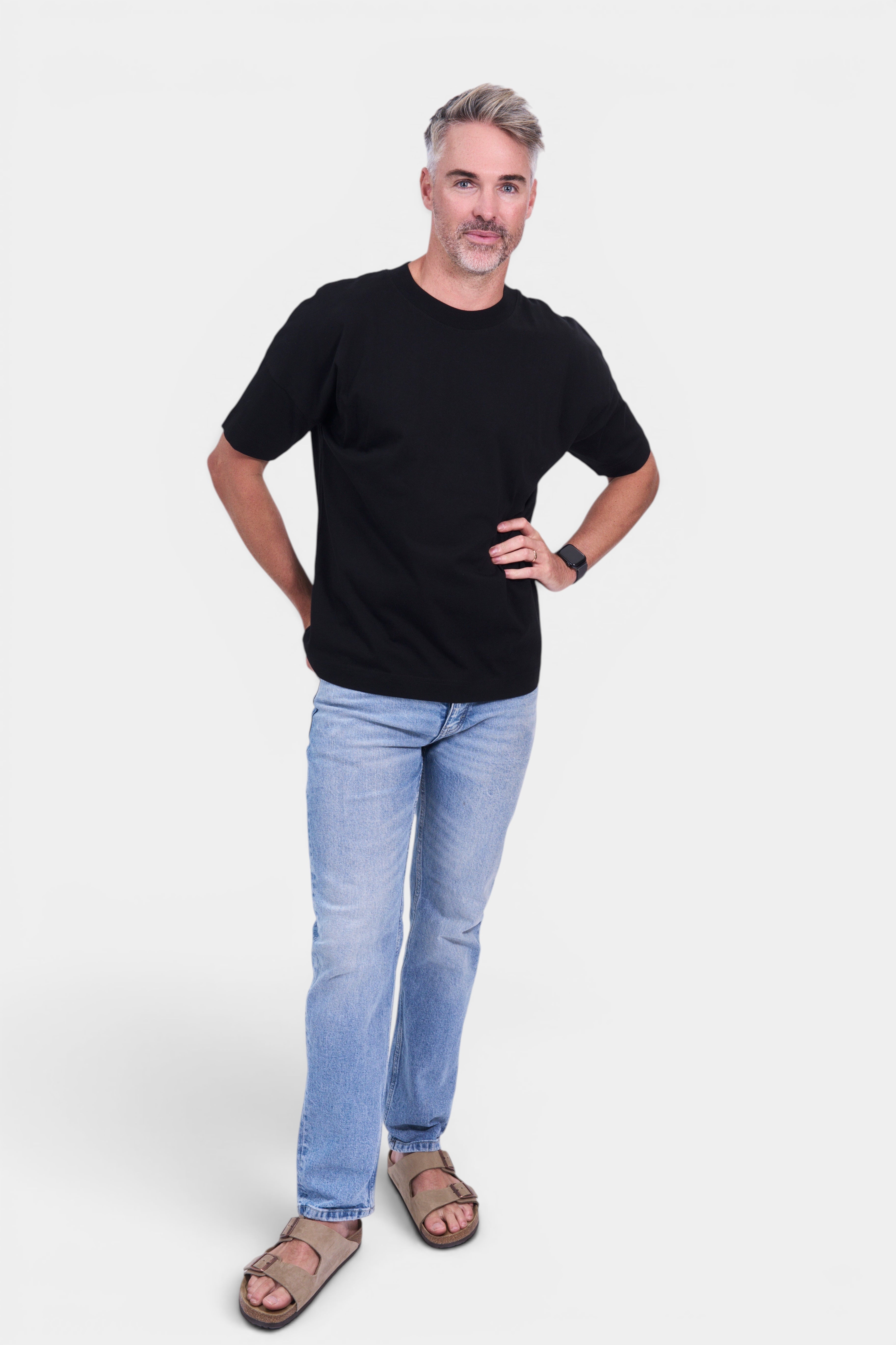 STAPLE Co black organic cotton classic fit tee on a man with light wash jeans and tan sandals.