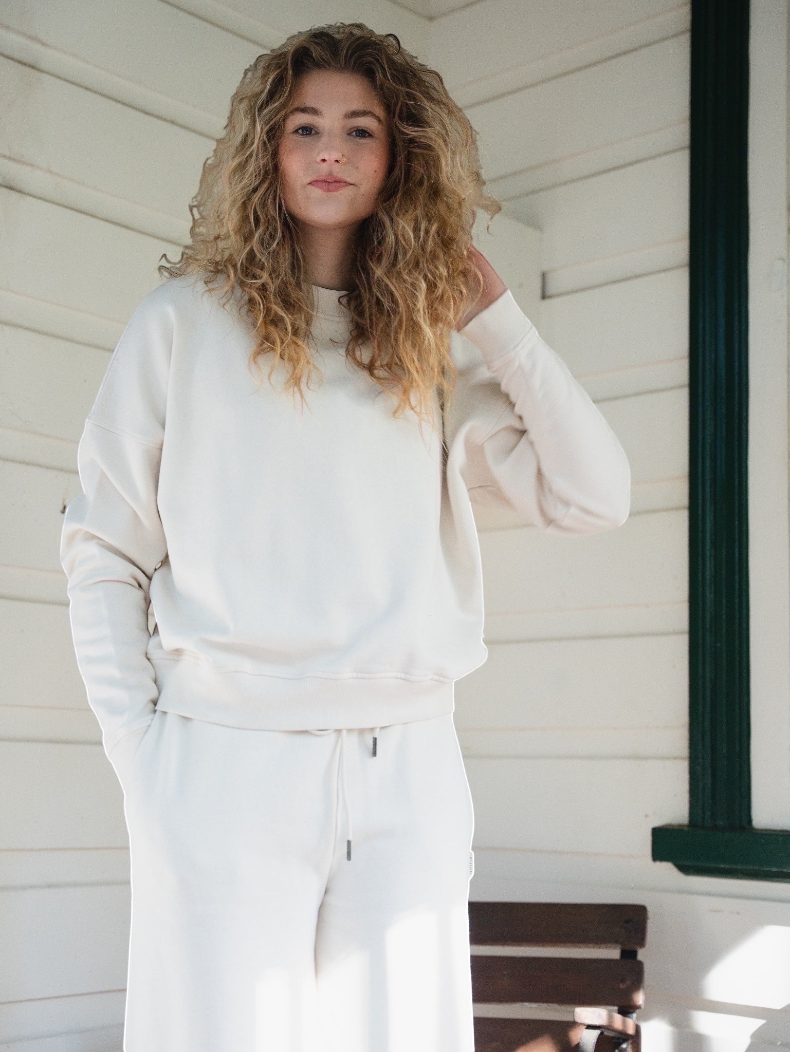 STAPLE Co boxy crewneck pullover in off-white organic cotton fleece worn by a woman with curly hair
