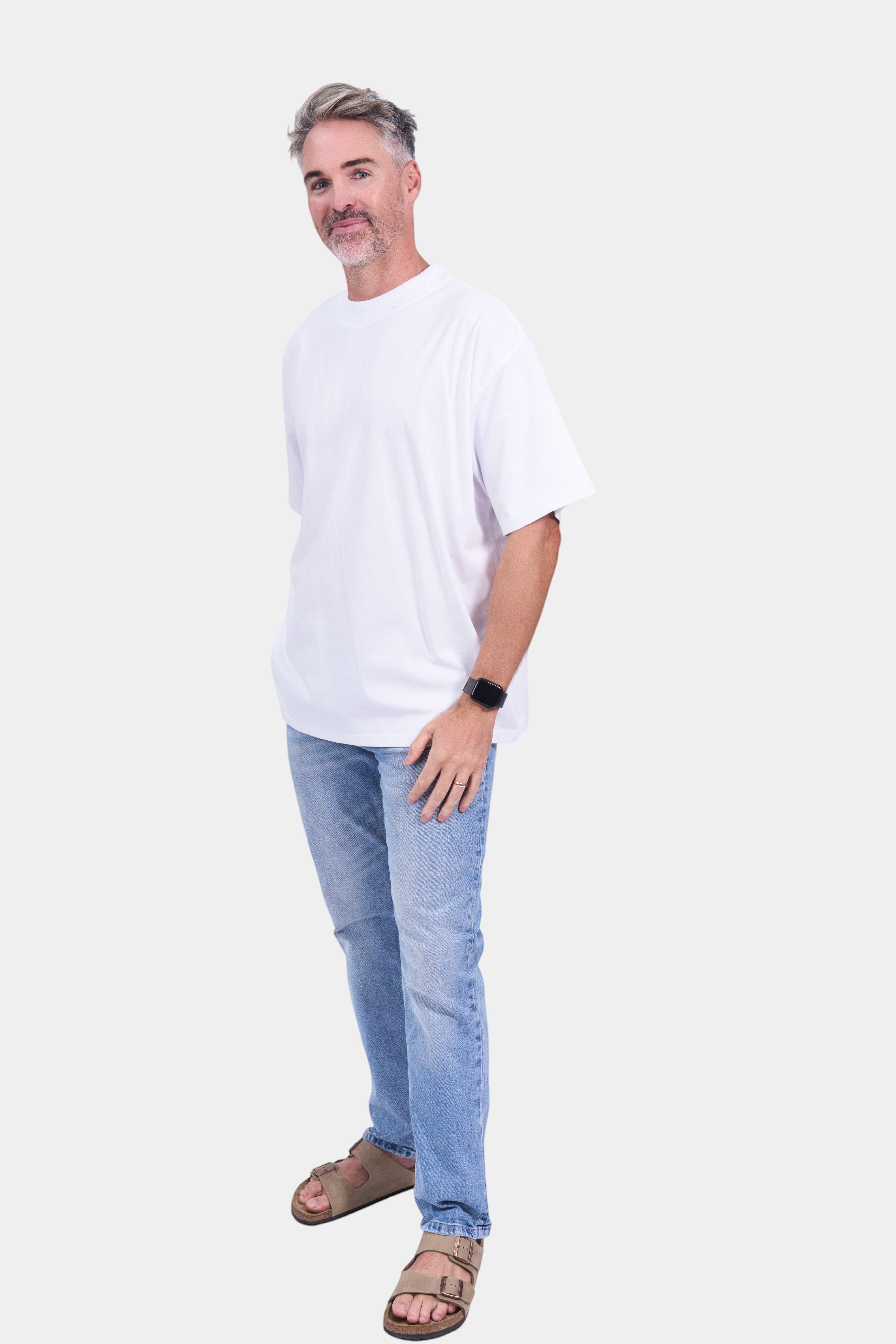 STAPLE Co white organic cotton high neck oversized t-shirt on a man with light wash jeans and sandals.